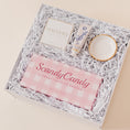 Load image into Gallery viewer, Lavender and Pine Sweet Surprise Gift Box angle view featuring Scandy Candy Swedish candy, Shinery radiance towelettes, Lanolips 101 ointment, and Apricity Ceramics gold rim ring dish in white luxe two piece gift box