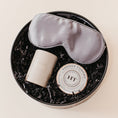 Load image into Gallery viewer, Lavender and Pine Ultimate Bliss Gift Box angle view featuring Pure Sol silk sleep mask, Minot candle, and Harney and Sons Vanilla Comoro tea tin in black round gift box