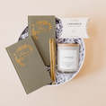 Load image into Gallery viewer, Lavender and Pine Written in Love Gift Box featuring Seniman Calligraphy olive vow books, gold ballpoint pens, Roote lavender candle, and McCrea's Cape Cod sea salt caramels in white round gift box