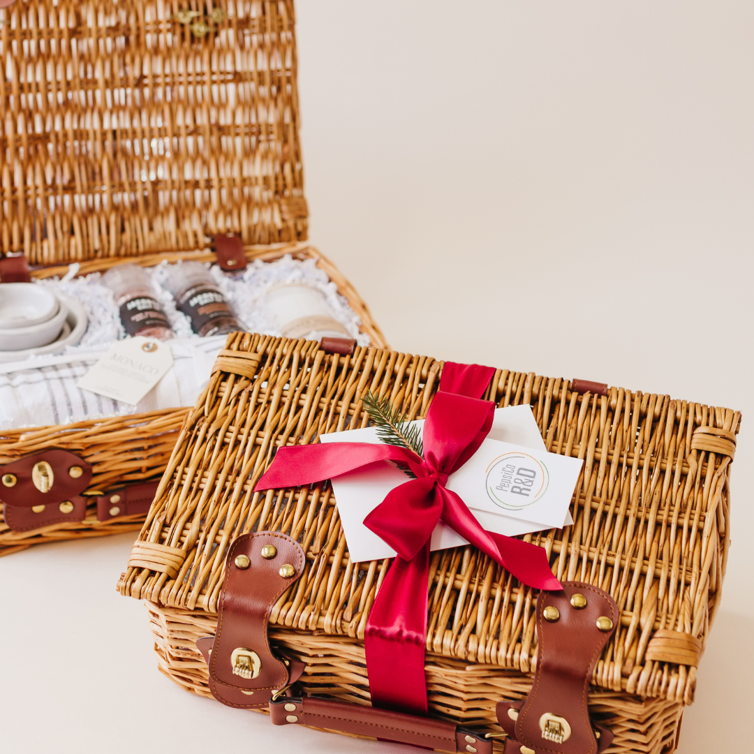 Two curated wicker gift baskets with custom branding tags and red ribbon bow, styled for corporate holiday gifting by Lavender and Pine.