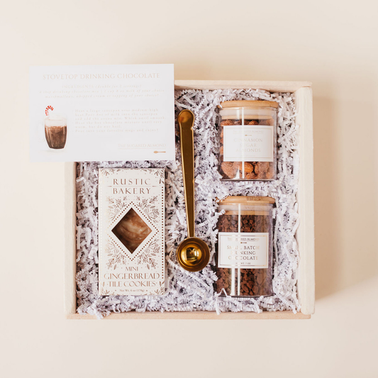 Corporate holiday gift box with gourmet hot chocolate, cinnamon sugar almonds, gingerbread cookies, and a gold scoop spoon, styled with crinkle paper in a wood box – perfect employee or client gift from Lavender + Pine.