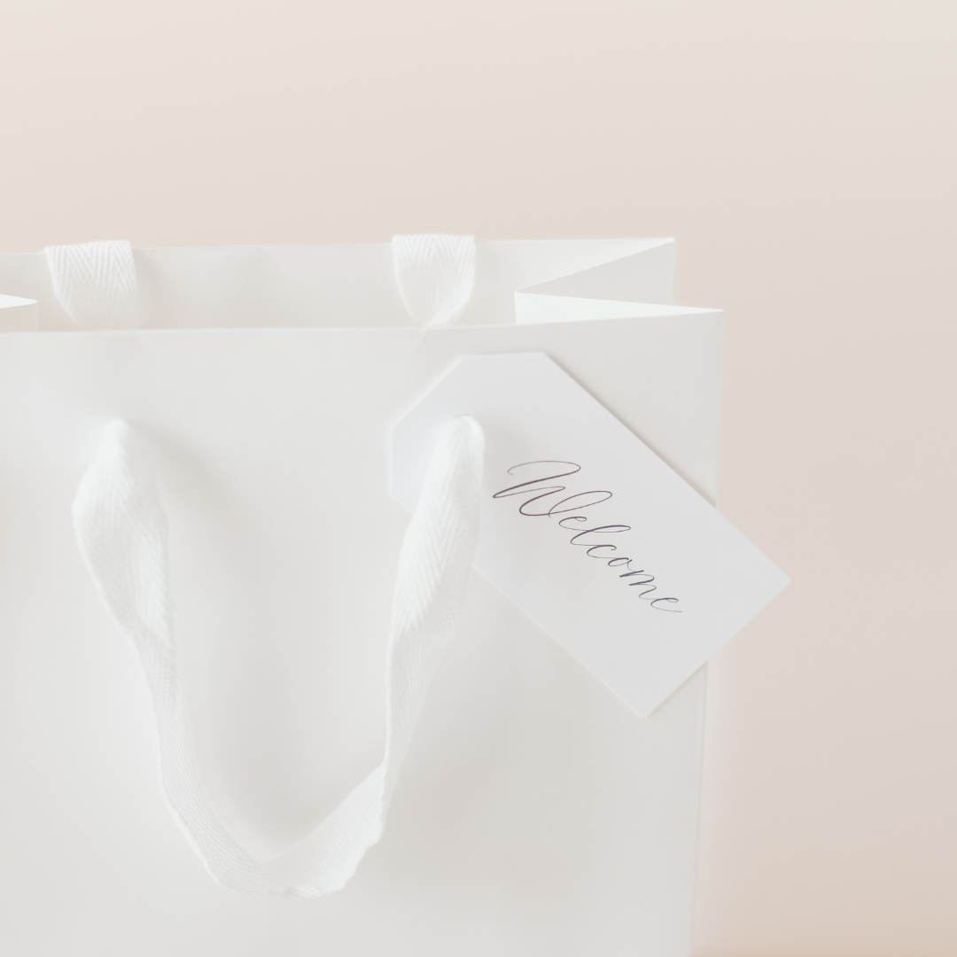 White wedding welcome gift bag with handwritten "Welcome" tag by Lavender + Pine, close-up of ribbon handles.