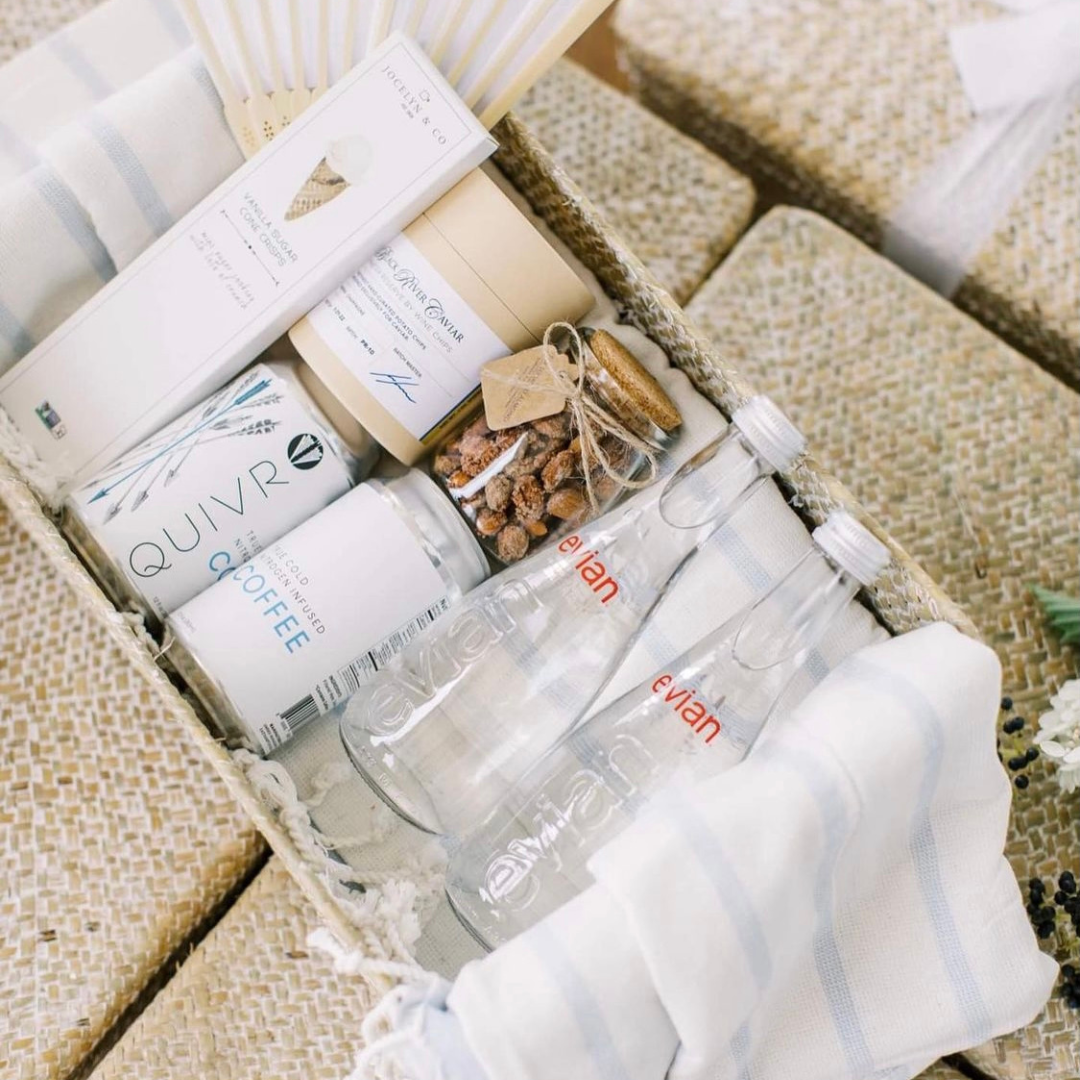 Curated wedding welcome gift featuring Evian water, cold brew coffee, local snacks, and thoughtful guest essentials in a woven basket  More experience-focused: