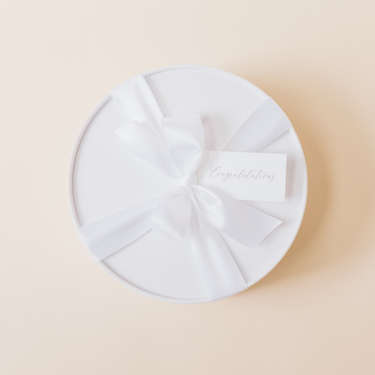 White round gift box with satin ribbon and congratulations tag – curated luxury gift packaging by Lavender + Pine