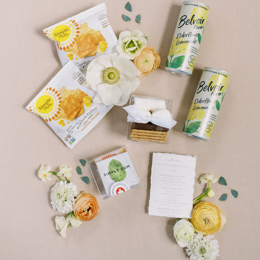 Close-up of rustic farmhouse wedding welcome gift box with elderflower lemonade, Simple Mills crackers, hangover kit, s’mores kit, and floral accents - curated by Lavender + Pine