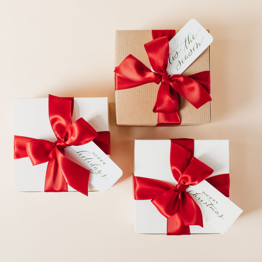 Elegant holiday gift boxes with red satin bows and calligraphy gift tags – luxury corporate and personal gifting by Lavender + Pine