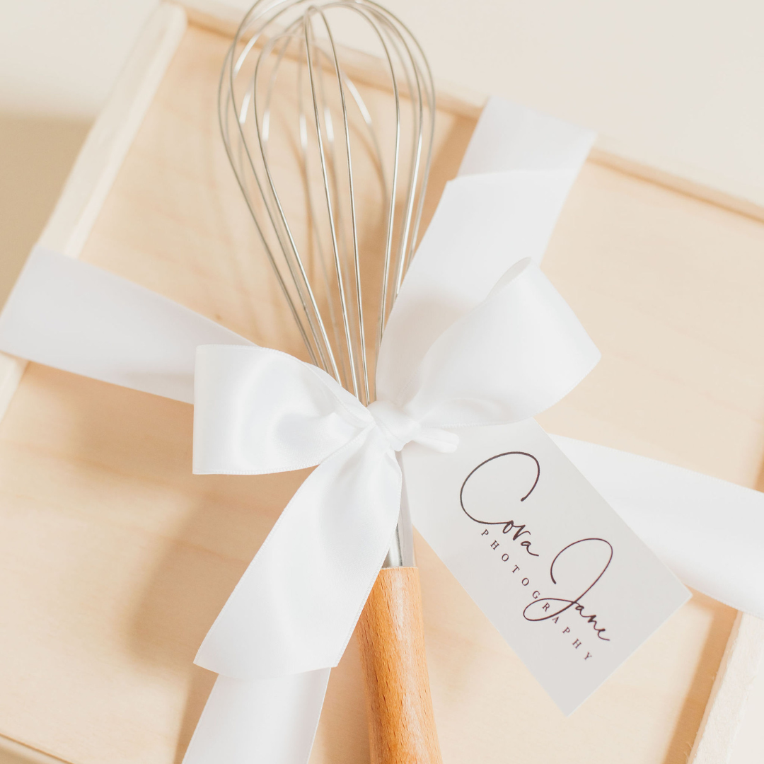 Minimalist client appreciation gift featuring a wooden whisk tied with a white ribbon and handwritten thank-you tag, styled to reflect thoughtful hospitality and intentional gifting