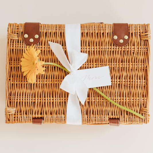 Wicker gift basket tied with a white ribbon and yellow flower, featuring a handwritten “Mom” tag - part of the Lavender + Pine Mother’s Day Culinary Collection.