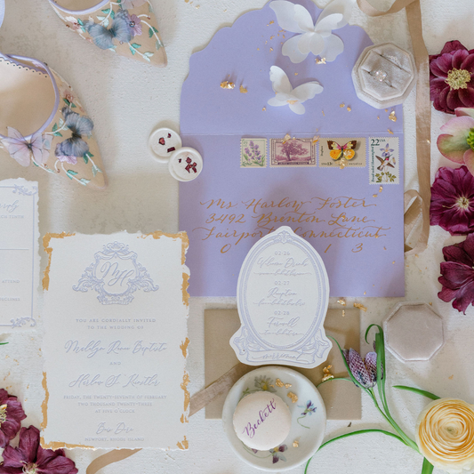 Flatlay of custom lavender wedding stationery, macaron favor, floral details, and calligraphy envelope styled by Lavender + Pine for a spring wedding in Newport, RI.