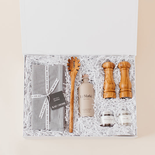 Lavender and Pine Entertainer's Kitchen Gift Box featuring Kaf Home grey linen napkins, Le Marké olive oil, Natural OliveWood pasta spoon, Natural OliveWood salt and pepper mills, and La Boite grey salt and Tellicherry pepper in white magnetic gift box