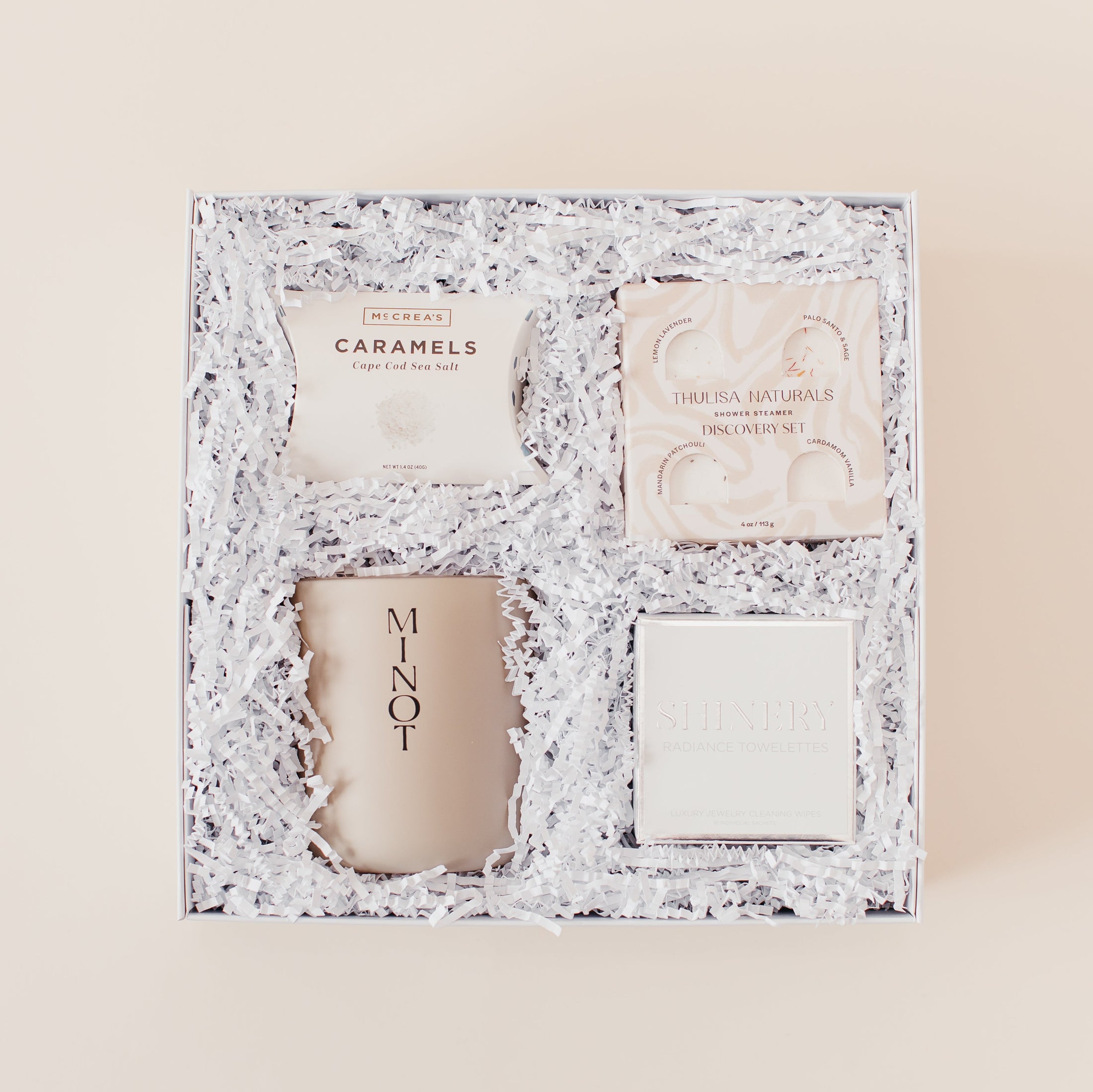 Lavender and Pine Refined Escape Gift Box featuring McCrea's Cape Cod sea salt caramels, Thulisa Naturals shower steamer discovery set, Minot Cliffwalk candle, and Shinery radiance towelettes in white luxe two piece gift box