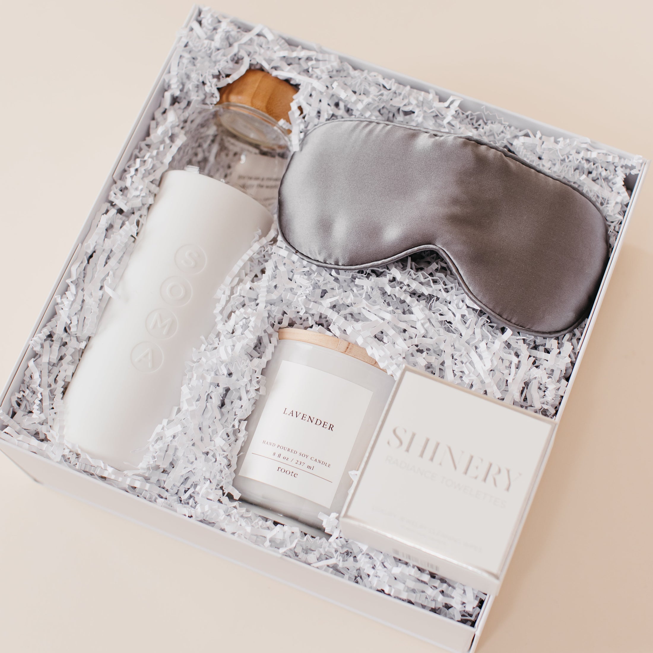 Lavender and Pine Rest and Restore Gift Box angle view featuring Soma glass water bottle, Pure Sol silk sleep mask, Roote lavender candle, and Shinery radiance towelettes in white luxe two piece gift box