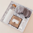 Load image into Gallery viewer, Lavender and Pine Soft Reset Gift Box angle view featuring Soma glass water bottle, Pure Sol silk sleep mask, ElizabethW lavender exfoliating shower pouch, and ElizabethW lavender shea butter hand cream in white luxe two piece gift box
