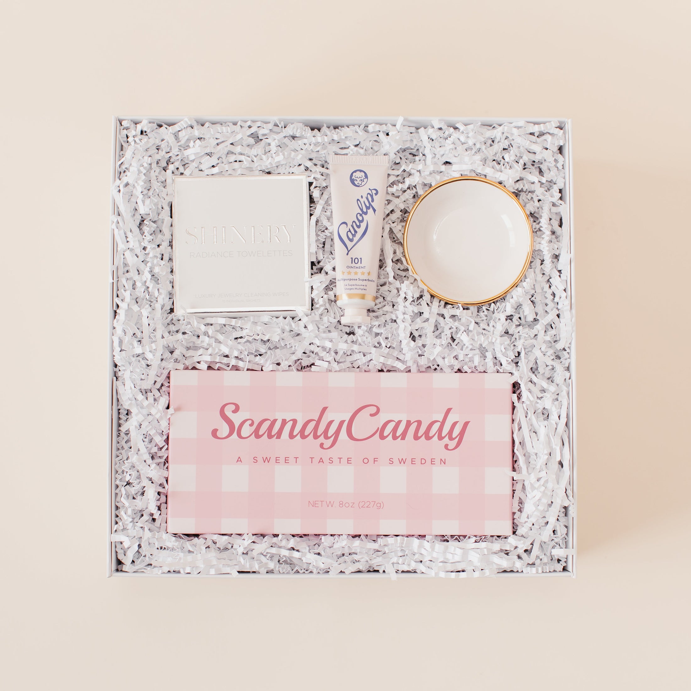 Lavender and Pine Sweet Surprise Gift Box featuring Scandy Candy Swedish candy, Shinery radiance towelettes, Lanolips 101 ointment, and Apricity Ceramics gold rim ring dish in white luxe two piece gift box