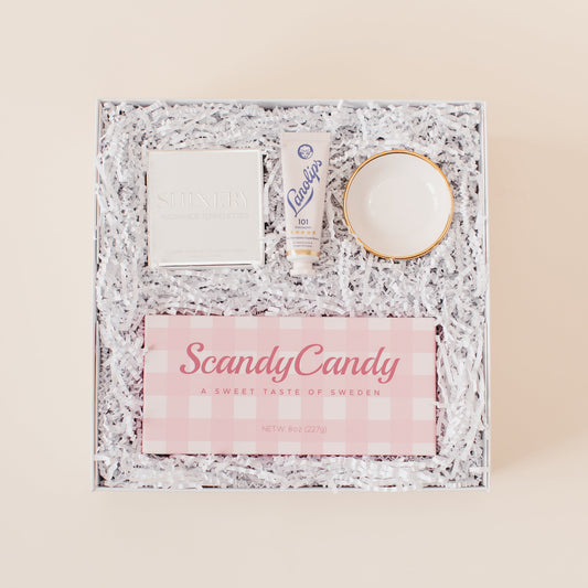 Lavender and Pine Sweet Surprise Gift Box featuring Scandy Candy Swedish candy, Shinery radiance towelettes, Lanolips 101 ointment, and Apricity Ceramics gold rim ring dish in white luxe two piece gift box